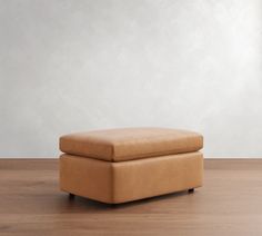 a tan ottoman sitting on top of a hard wood floor next to a white wall