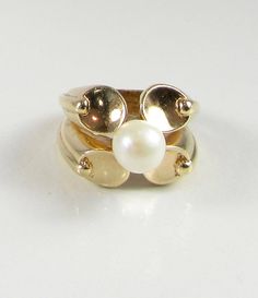 14 karat yellow gold pearl ring. The ring has 4 ovalish-round concave designs and the pearl sits in the middle of those designs. The pearl has a silvery white body color with little to no overtones. The width of the ring (north/south) measures approximately 15.50mm at its widest point. Ring Size: 6 can be sized Circa: Late 1970's early 1980's All rings come with one free sizing...To size the ring down it is completely free...to size the ring up we will pay for the first size, and you will pay th Heirloom Style Gold Pearl Ring With Polished Finish, Oval Gold Pearl Ring, Oval Yellow Gold Pearl Ring, Oval Pearl Ring In Yellow Gold, Antique Gold Oval Pearl Ring, Modern Oval Pearl Ring For Anniversary, Heirloom Pearl Ring With Polished Finish, Vintage Gold Oval Pearl Ring, Pearl Rings Vintage