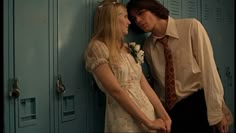 two people standing next to each other in front of lockers with one woman touching the man's forehead