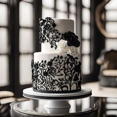 a white and black wedding cake with flowers on top is sitting on a table in front of large windows