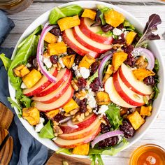 a salad with apples, cranberries and walnuts in a white bowl on top of a wooden table