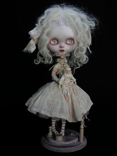 a doll with white hair and red eyes wearing a dress on top of a wooden stand