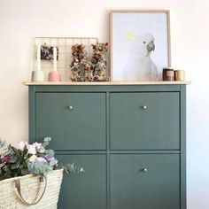 a white bird sitting on top of a green cabinet next to a basket with flowers