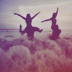 two women are in the ocean with their arms up and one is holding her hands out