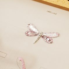 a pink and white dragonfly brooch sitting on top of a piece of paper