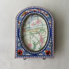 an ornate blue and white frame with flowers on it's sides is hanging from the wall