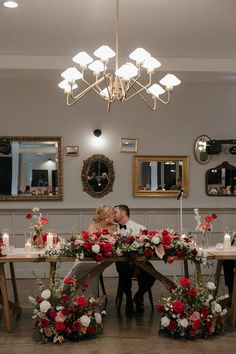 a man and woman sitting at a table with flowers on it, surrounded by candles