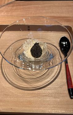 a glass bowl filled with food on top of a wooden table next to a spoon