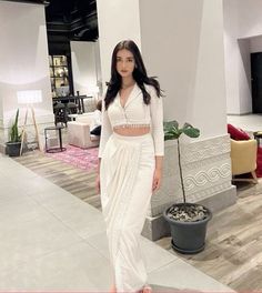 a woman standing in front of a white wall wearing a long skirt and crop top