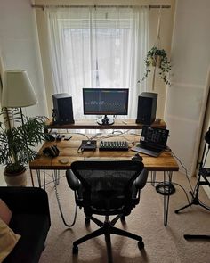 a computer desk sitting in front of a window next to a black chair and potted plant