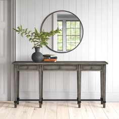 a table with a mirror and vase on it in front of a white painted wall