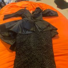 an orange and black dress laying on top of an orange bed sheeted with other clothes