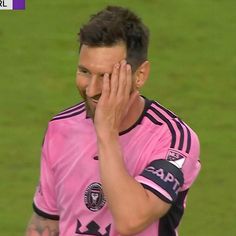 a soccer player wiping his face with one hand and looking at the camera while standing on a field