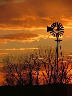 the sun is setting behind a windmill and trees