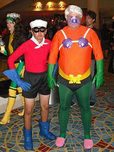 two men in costumes standing next to each other on a carpeted floor with people dressed as cartoon characters