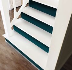 a white and blue book shelf sitting on top of a hard wood floor next to a stair case