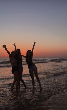 three girls are standing in the water at sunset on the beach with their arms up