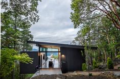 a black house in the woods with trees around it and people standing on the porch