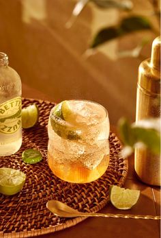 a close up of a drink on a table with limes and a shaker