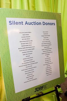 a sign that says silent auction donors in front of green curtained walls and floor