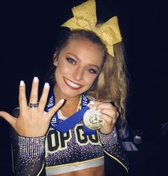 a cheerleader holding up her gold medal and posing for the camera with her peace sign