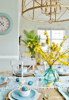 a dining room table is set with blue and white plates, silverware, and yellow flowers