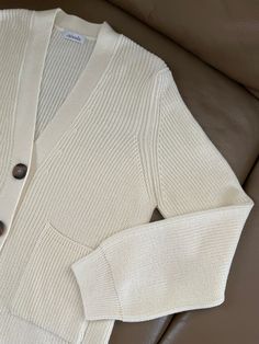 a white cardigan sweater with buttons on the front and back, sitting on a brown leather couch