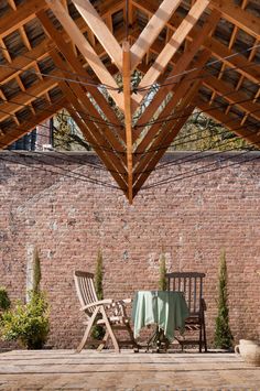 two chairs and a table under a wooden roof over an outdoor patio with brick walls