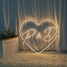 a heart shaped neon sign sitting next to a potted plant