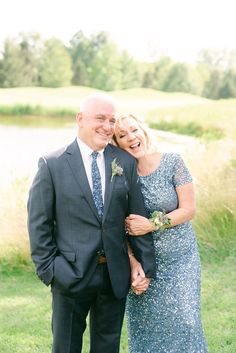 a man and woman standing next to each other in front of a lake wearing formal attire