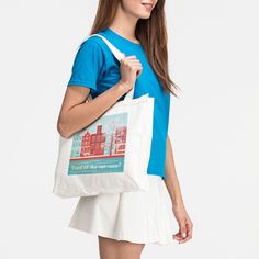 a woman is holding a white bag with a city scene on it