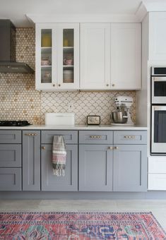 a kitchen with white cabinets and gray counter tops, an area rug on the floor