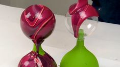 two colorful vases sitting next to each other on a white counter top, one is green and the other is pink