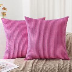 two pink pillows sitting on top of a couch next to a vase filled with flowers