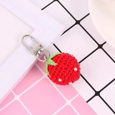 a crocheted strawberry keychain on a pink and white tiled surface