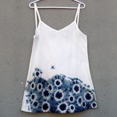 a tank top with blue and white flowers on it hanging from a clothes line against a gray wall