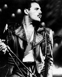 a black and white photo of a man in leather jacket holding a microphone on stage