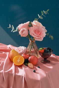 a vase filled with pink roses sitting on top of a table covered in fruit and veggies