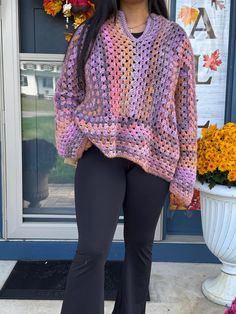 a woman standing in front of a door wearing black pants and a purple crochet sweater