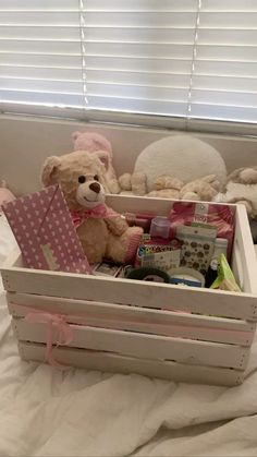 a teddy bear sitting in a wooden crate filled with baby items on a white bed