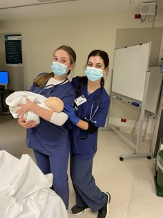 two women in scrubs and masks holding a baby