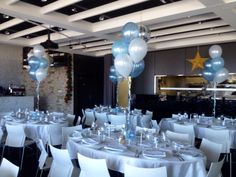 a room filled with tables and chairs covered in white tablecloths topped with blue and silver balloons