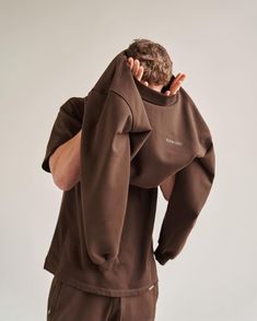 a man wearing a brown sweatshirt and sweatpants is covering his face with his hands