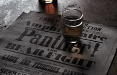 a glass of beer sitting on top of a newspaper next to a bottle of liquor