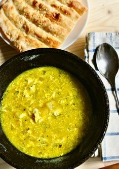 there is a bowl of soup on the table next to some bread and spoons