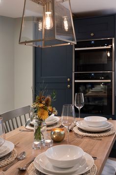 a wooden table topped with white plates and silverware next to a light fixture above it