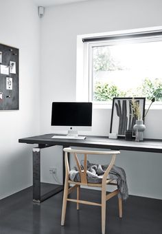 a desk with a computer on it in front of a window and some pictures hanging on the wall