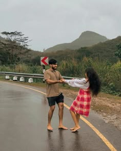 a man and woman standing on the side of a road in the rain holding hands