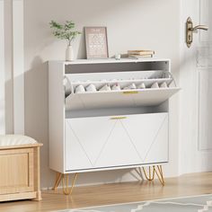 a white cabinet with gold legs in a living room next to a rug and potted plant