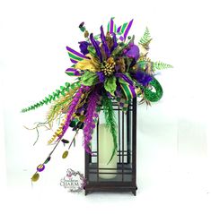 a tall glass vase with purple and green flowers in it's centerpiece on a white background